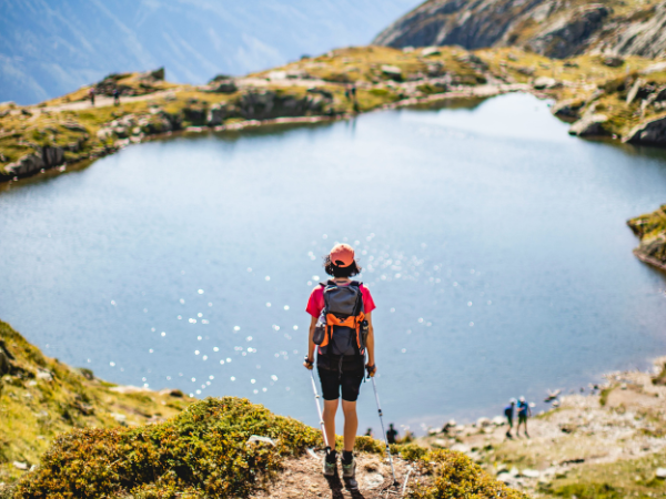 A woman hiking looks over a beautiful lake vista, to illustrating how to be happy