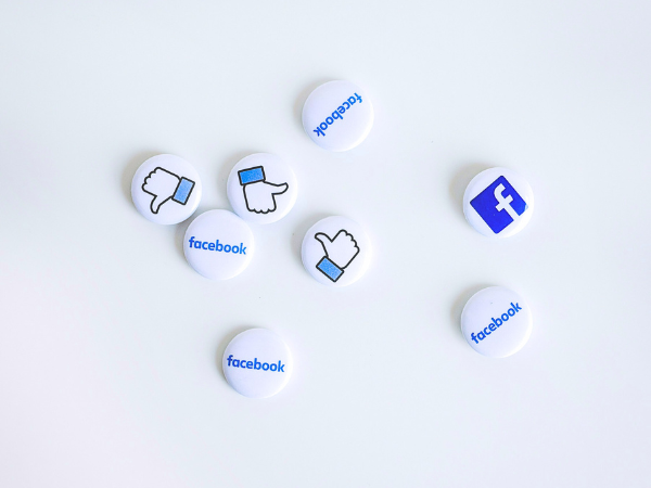 Several facebook buttons and badges lay scattered on a white table, to illustrate the Facebook Algorithm