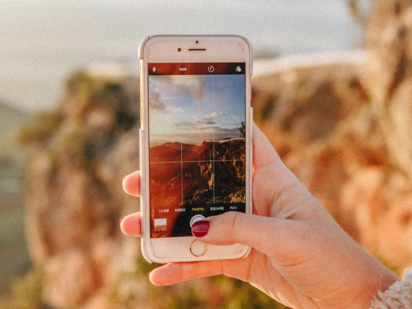 woman's hand holding an iphone, taking a photo of a rocky landscape, to illustrate creating content to grow on Instagram