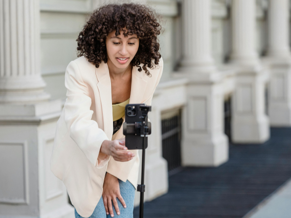 a woman in a white blazer sets up her phone on a tripod to record a video to illustrate Instagram Trending reels