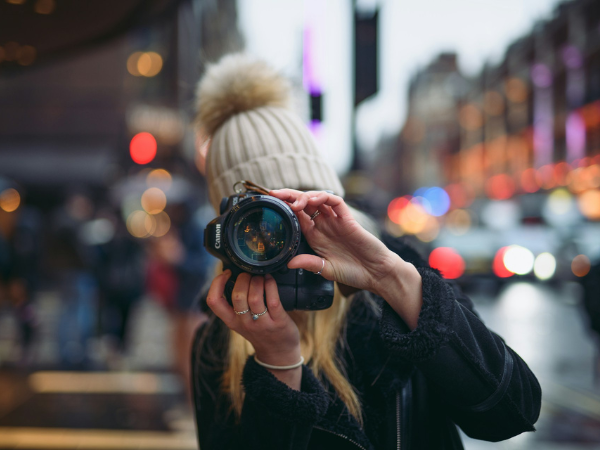 A woman in a beanie takes a photo on a rainy street to illustrate finding the best Social Media Image Sizes