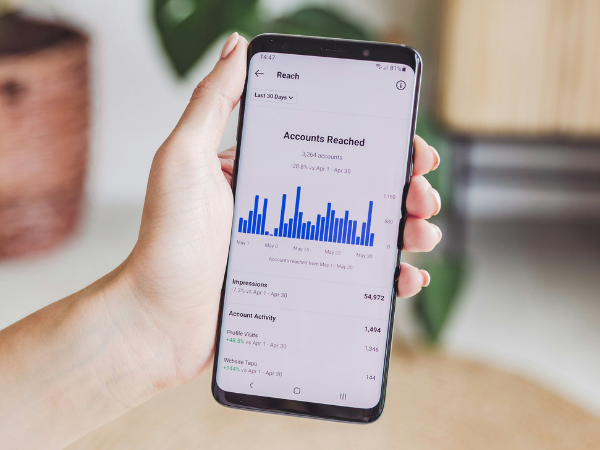 A hand holds a phone with a view of Instagram's social media metrics open on the screen